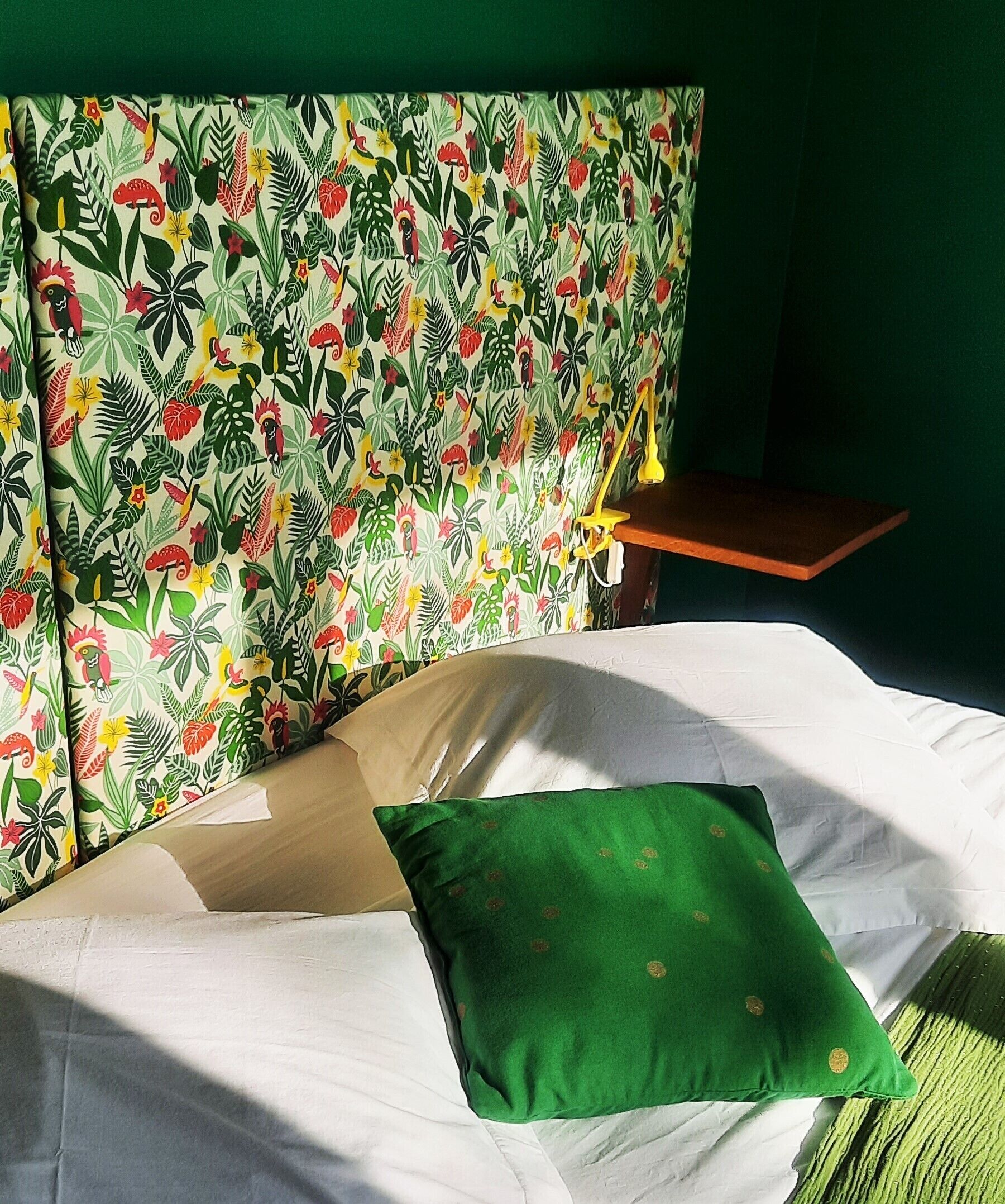 A bed with a floral-patterned headboard, a green pillow, and a wooden nightstand with a lamp.