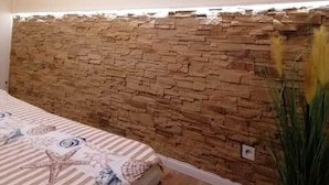 A bedroom with a stone headboard, a bed with striped bedding, a framed picture of a beach, and a potted plant.