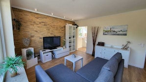 A modern living room with a stone wall, a flat-screen TV, a grey sofa, a small coffee table, and a white cabinet.