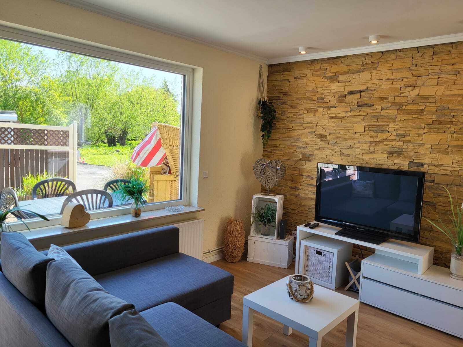 Un salon moderne avec un mur en pierre, une grande fenêtre, un canapé gris, une table basse blanche et un téléviseur à écran plat.