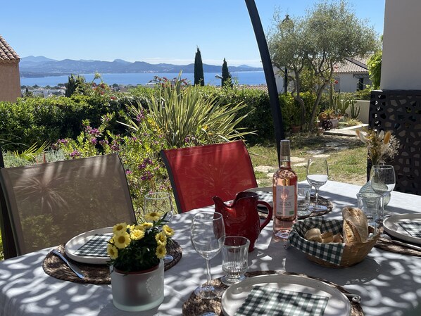 Un área de comedor al aire libre con una mesa dispuesta para dos personas, que incluye una botella de vino, copas y una cesta de pan.