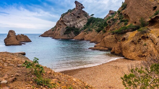 Un paysage côtier caractérisé par des falaises rocheuses, une mer d’un bleu limpide et une plage de galets.