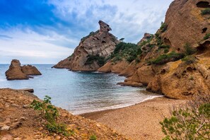 Un paisaje costero con acantilados rocosos, mar azul cristalino y una playa de guijarros.