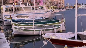 Un port de plaisance avec des bateaux amarrés, un bâtiment historique doté d’une tour et un ciel dégagé.