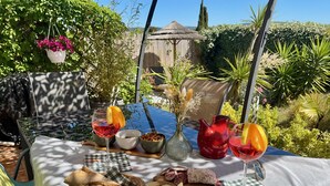 Une table de jardin, dressée à l’extérieur avec de la nourriture et des boissons, entourée de verdure et d’une clôture en bois.