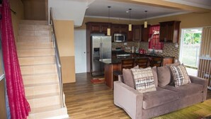 Amplia sala de estar con sofá, escalera y cocina equipada con electrodomésticos modernos.