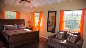 Un dormitorio con cama de madera, sofá, ventana grande con cortinas, ventilador de techo y espejo.