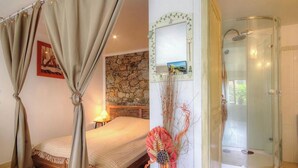 Een slaapkamer met een bed, een stenen muur, een decoratief wandobject en een douche met glazen wanden.