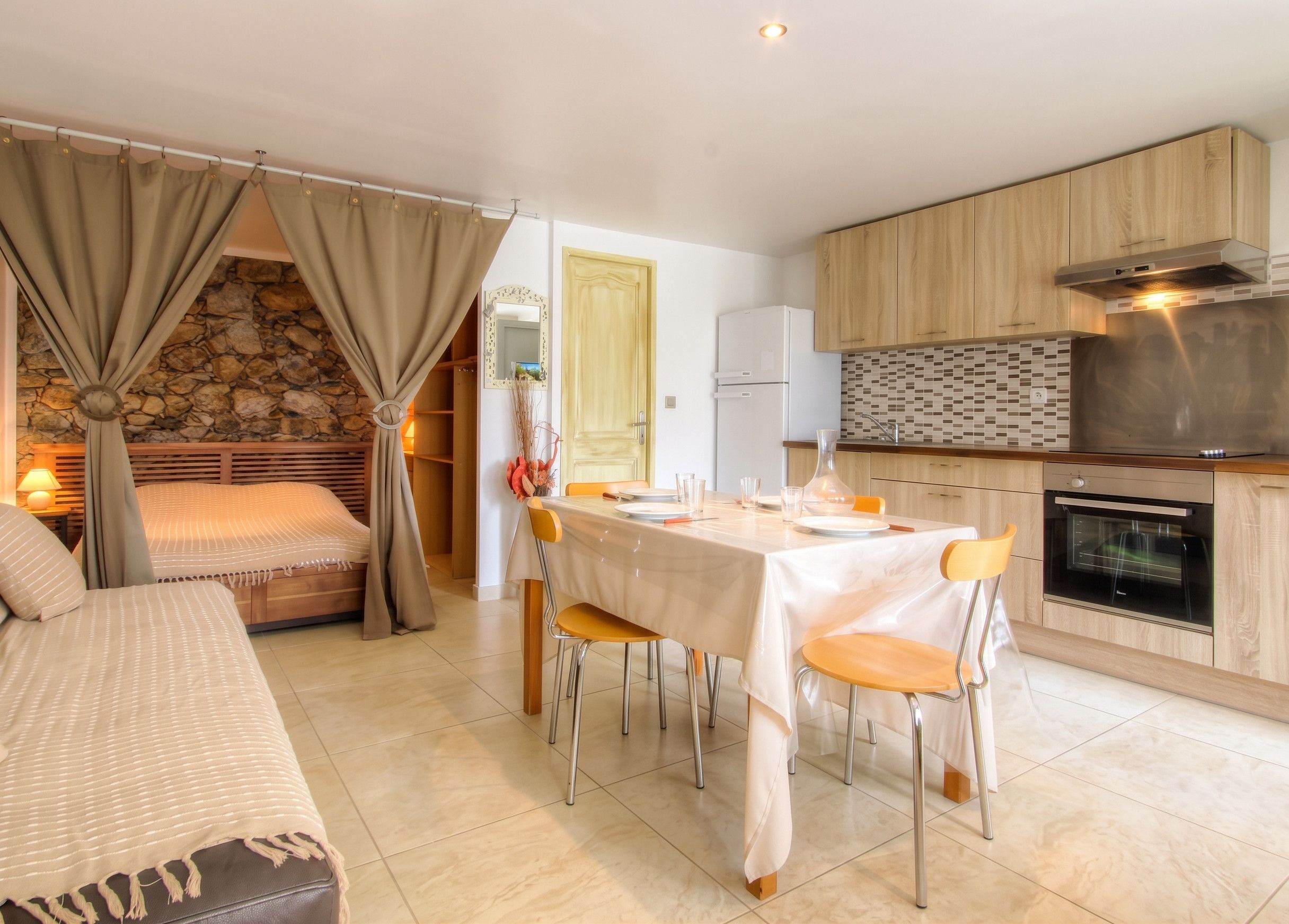 Une cuisine moderne avec un coin repas, un mur en pierre et un lit agrémenté de rideaux.