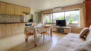 Een moderne keuken met houten kastjes, een eettafel met stoelen, een televisie op een standaard en een bank.