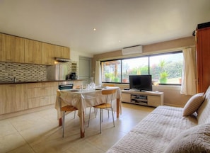 Une cuisine moderne avec des meubles en bois, une table à manger avec des chaises, un téléviseur posé sur un meuble et un canapé.