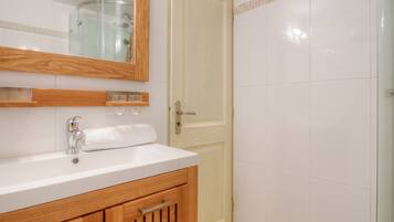Une salle de bain avec un lavabo blanc, un meuble-lavabo en bois, une cabine de douche en verre et une porte dotée d’une poignée.