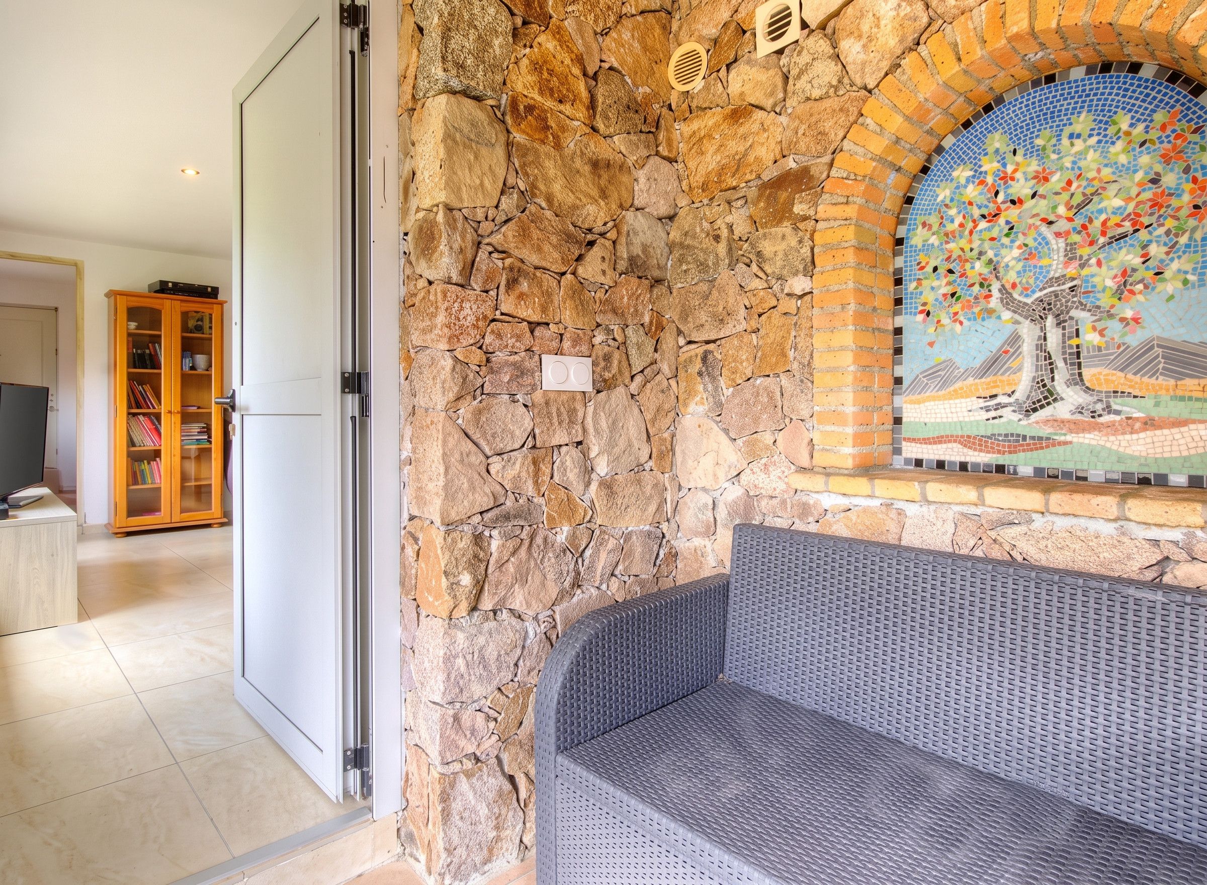 A stone wall with a mosaic, a bench, and a bookshelf in a room.