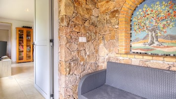 A stone wall with a mosaic, a bench, and a bookshelf in a room.