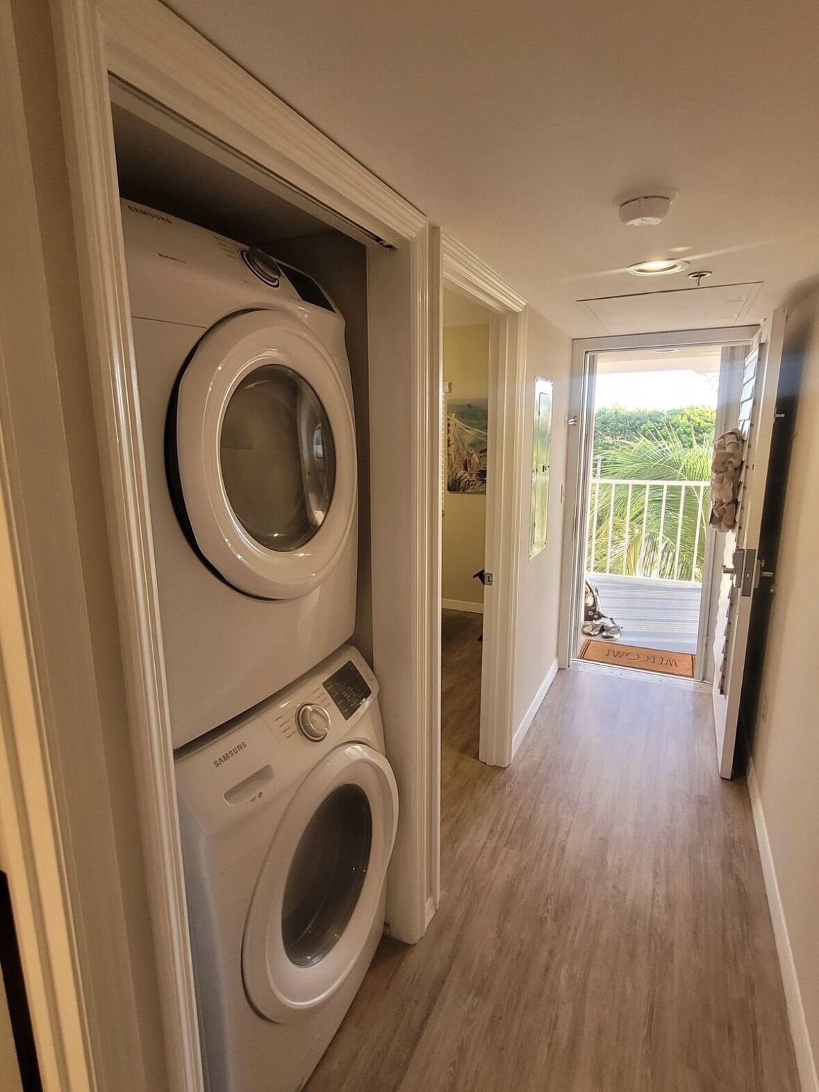 A laundry room with stacked washers and dryers, a wooden floor, and a view of a balcony with greenery.