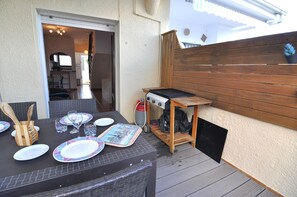 An outdoor patio with a grill, dining table set with plates and cutlery, and a wooden fence.
