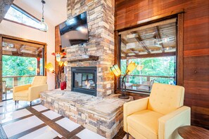 Cozy seating area with a stone fireplace, flat-screen TV, and a large window offering a view of the outdoors.