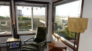 Ett rum med utsikt över stranden, en grön stol, ett litet bord och en lampa.