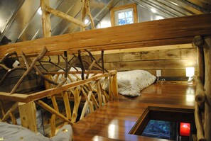 Un dormitorio estilo loft con una escalera de madera, una cama con almohada blanca y un ventanal pequeño.