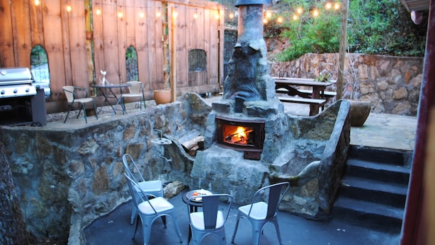 Une terrasse extérieure avec des murs en pierre, un foyer et des chaises en métal.