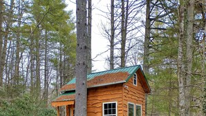 Une cabane en bois, accessible par un sentier de pierres, et entourée d’arbres.