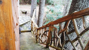 Un escalier en bois, au design rustique et naturel, mène à un sentier de pierres entouré d’arbres.