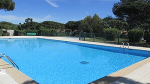 Una piscina rectangular con superficie de agua azul cristalina, rodeada por una solería azulejada y una cerca de metal.