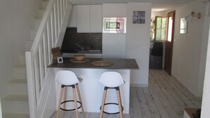 Cocina compacta con una isla central, dos taburetes de bar y una escalera que sube a un nivel superior.