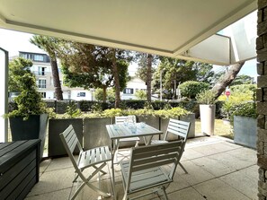 An outdoor patio with a table and chairs, surrounded by planters and a view of residential buildings.