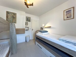 A bedroom with a wooden headboard, a bed with a white mattress and blue pillow, a small bedside table, and a wall-mounted light fixture.