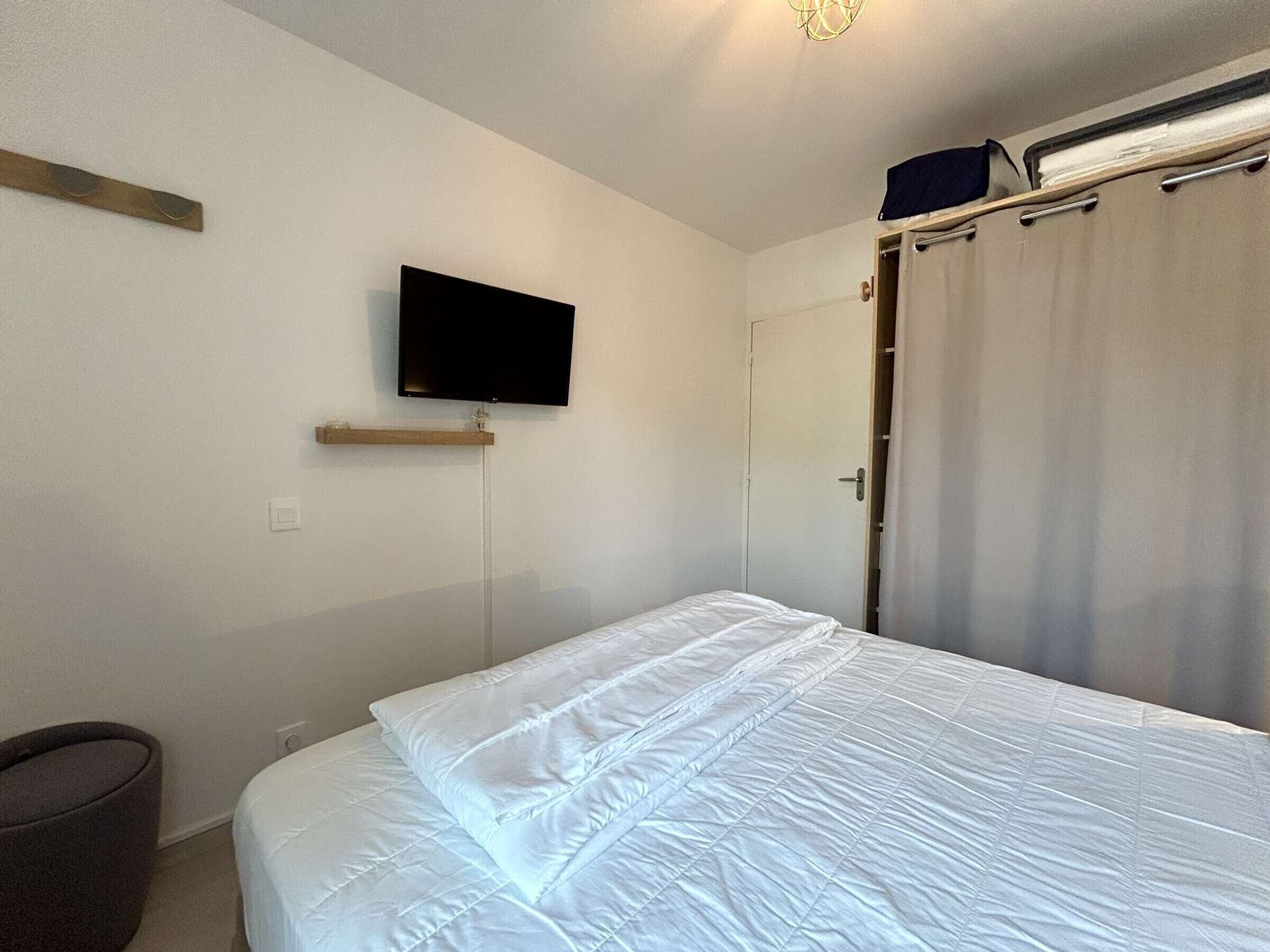Una camera da letto con un letto, una televisione a muro, una porta e una tenda.