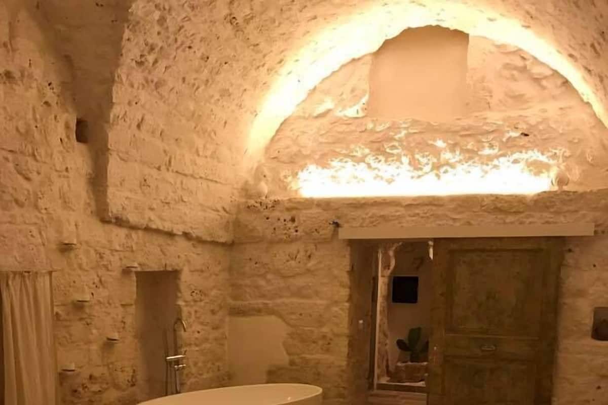 A bedroom with a large bed, a bathtub, and a stone wall.