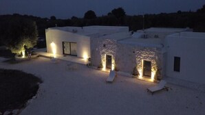 Una villa moderna con patio, que cuenta con piscina, tumbonas y una entrada bien iluminada.