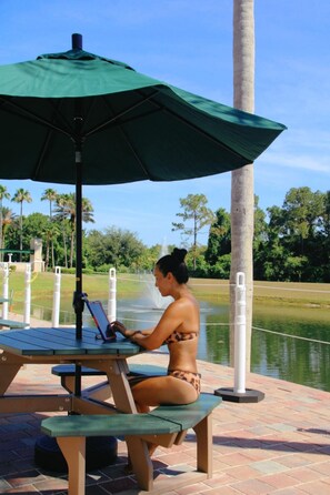 A person sitting at a table under a green umbrella, using a laptop. - Pet Friendly 3-bedroom townhouse  so close to Disney you can hear the fireworks! (Kissimmee)