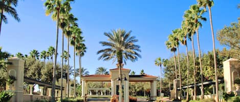 A gated entrance with palm trees, a covered walkway, and a clear blue sky.