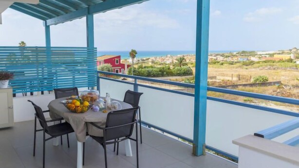 A balcony with a table set for two, overlooking a coastal landscape.