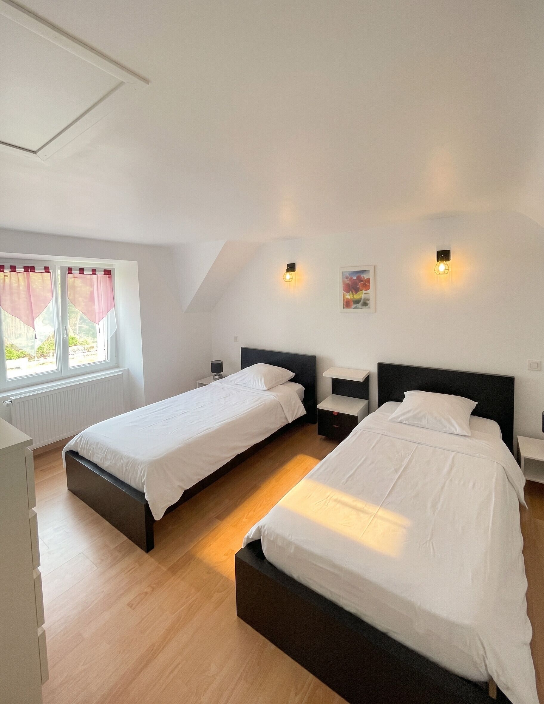 A bedroom with two beds, a window with curtains, bedside lamps, and a painting on the wall.