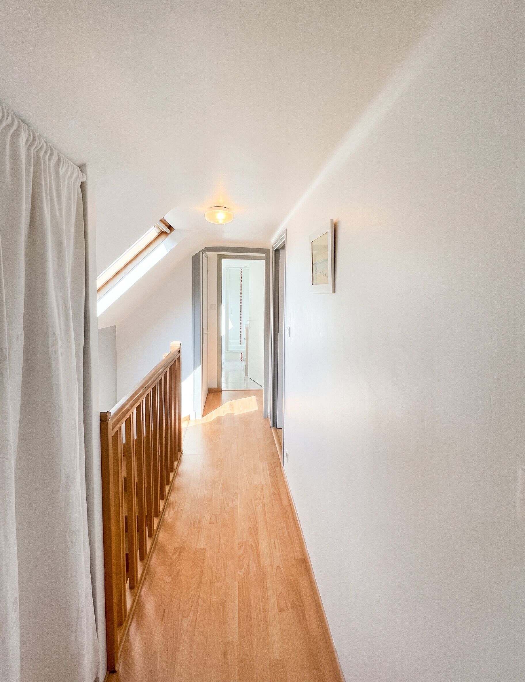 Un corridoio con pavimento in legno, pareti bianche, ringhiera in legno e una lampada a soffitto.