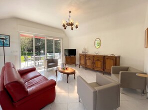 Un salon spacieux avec un canapé rouge, un fauteuil gris, un meuble en bois et un téléviseur.