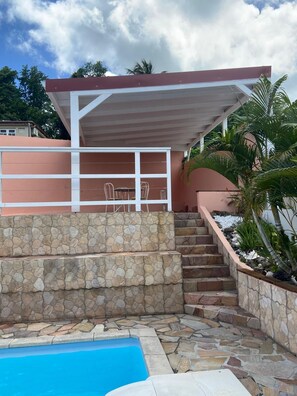 A pool area with stone steps and a covered seating area with chairs.