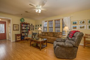 A living room with a brown leather sofa, a wooden coffee table, a bookshelf, and a ceiling fan. - Across from Dollywood w/ FREE Dollywood ticket, pets ok w/fee, arcade, hot tub (Pigeon Forge)
