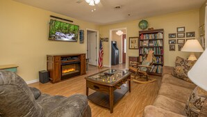 Una sala de estar con chimenea, televisor, estantería y ventilador de techo.