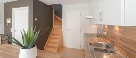 A modern kitchen with wooden flooring, a built-in sink, and a staircase leading to another level.