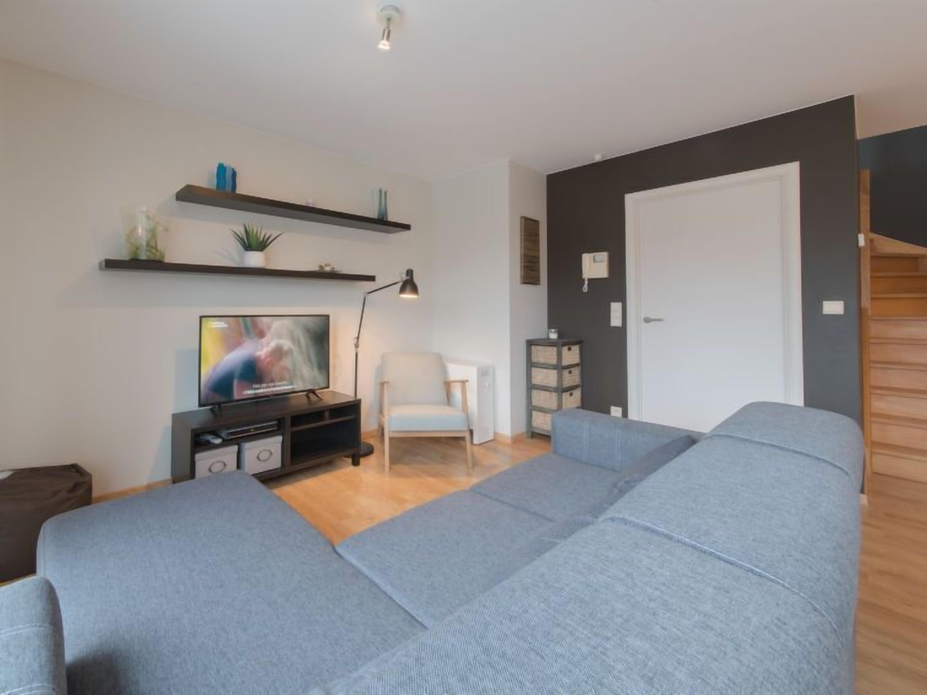 Un soggiorno moderno con un divano grigio, una TV su un mobile, una poltrona bianca e un tavolino con oggetti decorativi.
