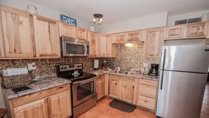 Una cocina con armarios de madera, un refrigerador de acero inoxidable, un microondas, un horno y una encimera de granito.