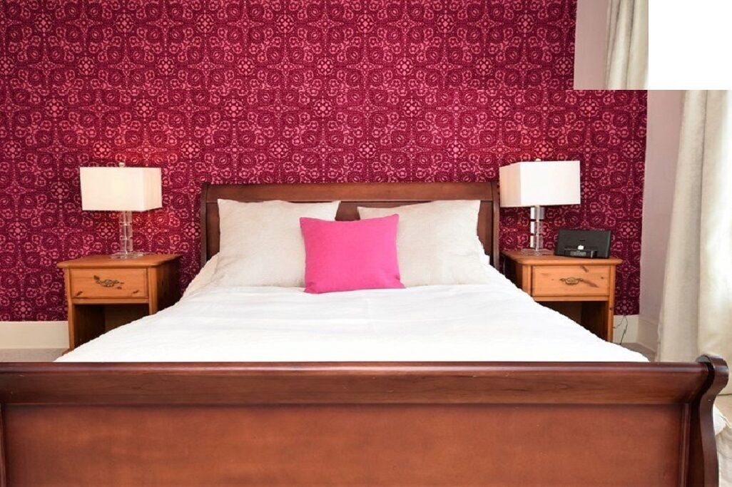 Een net opgemaakt bed met wit en roze beddengoed, omringd door twee nachtkastjes met lampen, voor een behang met patroon.