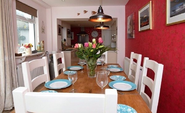A dining room with a wooden table set for six, white chairs, and a vase of flowers.