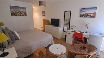A bedroom with a bed, a desk, a chair, a television, and a mirror.