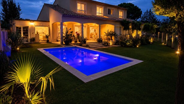 Une maison à deux étages avec une piscine, entourée d’une pelouse bien entretenue et de plantes en pot.