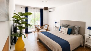 Une chambre à coucher avec un lit, des tables de chevet, une chaise, une plante et une vue sur l’extérieur.